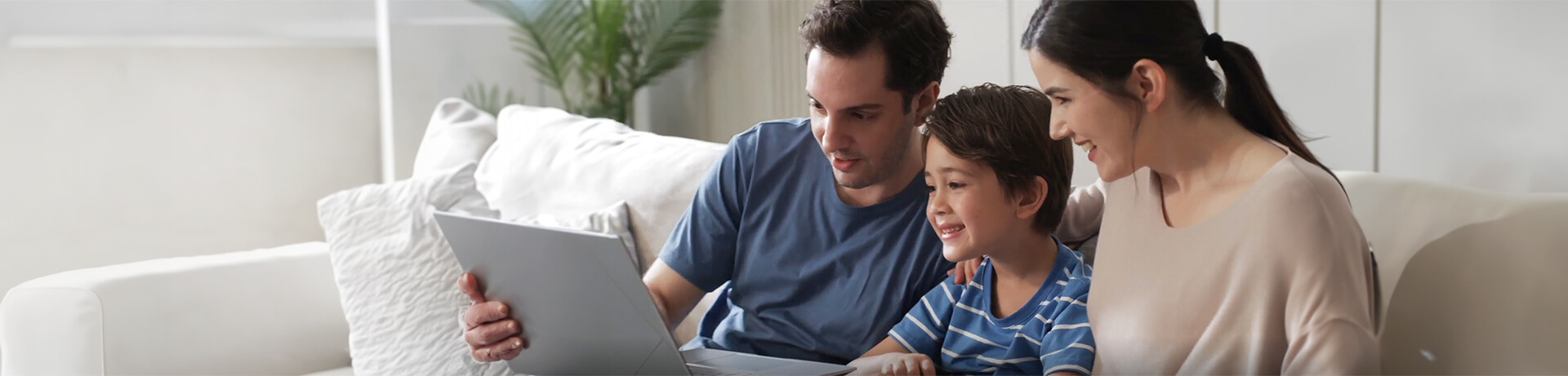 Parents and a boy sitting on a couch and looking at a laptop together, smiling and engaged.