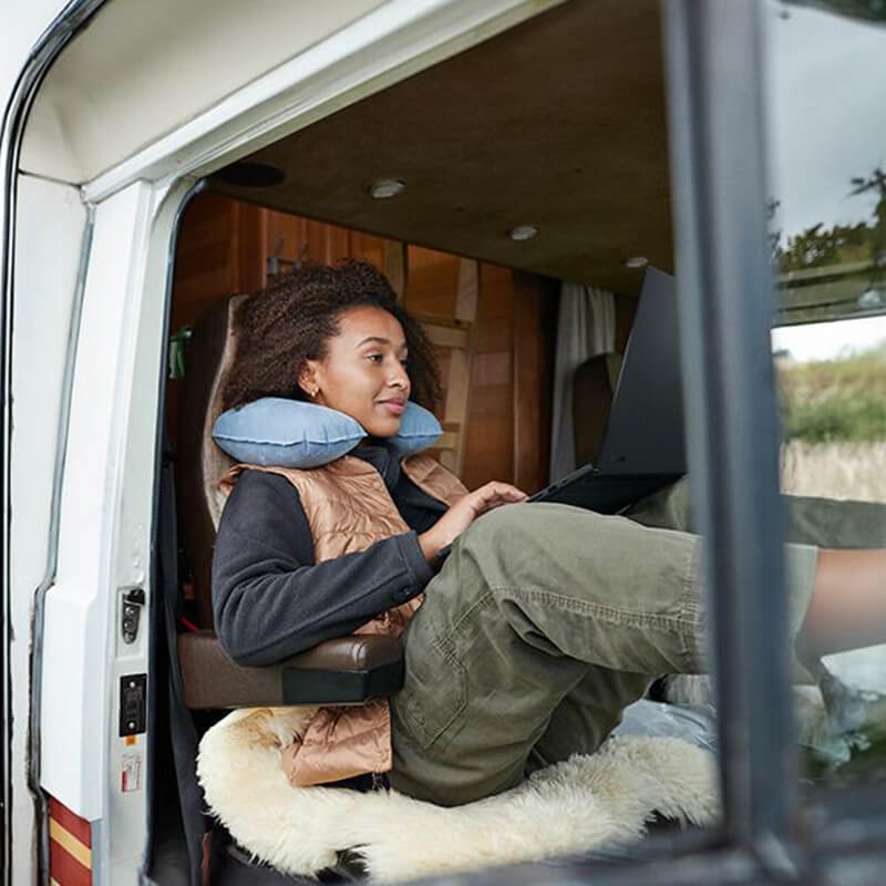 A woman is laid back in her van and using a ProArt P16 laptop with her legs propped up on the dashboard.