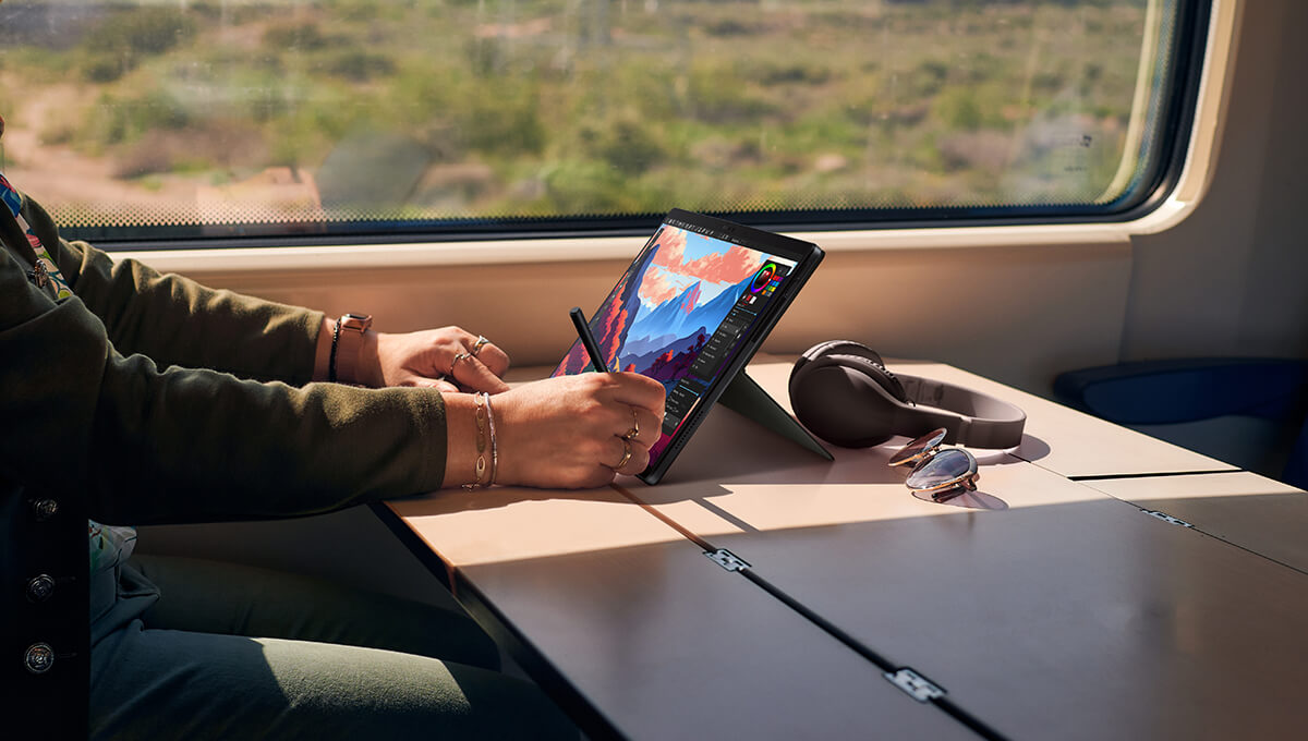 a content creator editing an image by using a stylus on the ProArt PZ13 laptop-and-tablet device on a table on a train