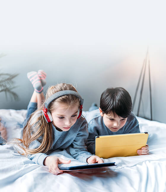 Zwei Kinder liegen auf einem Bett und benutzen ihre Tablets.