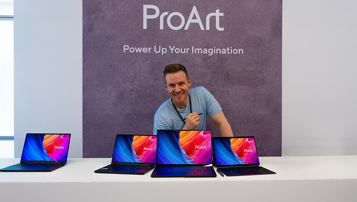 Jazza smiles holding a stylus behind three ProArt laptops.