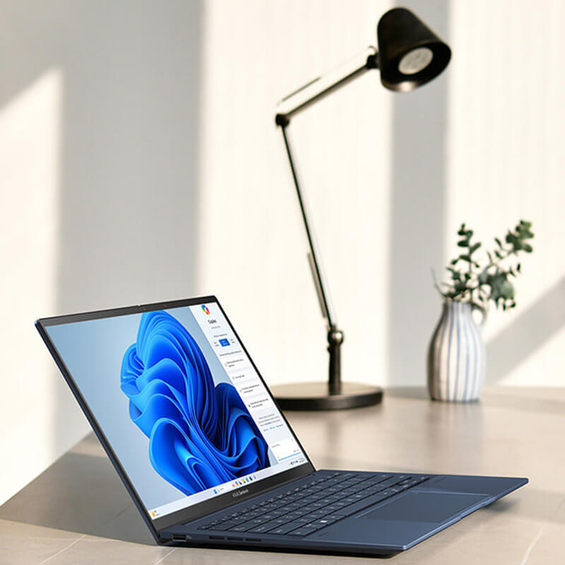 ASUS Zenbook 14 OLED sitting on a stone desk with Microsoft Copilot displayed on the screen