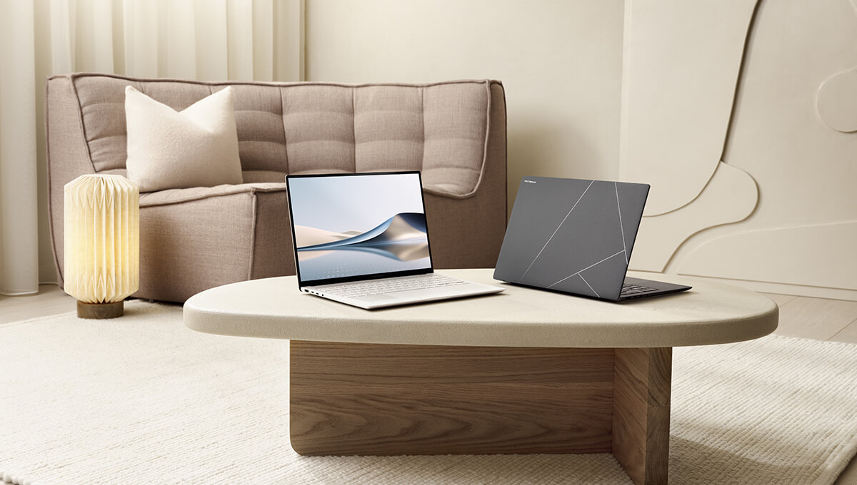 Two Zenbook S 16 laptops are placed on a beige colored table in a modern looking living room.