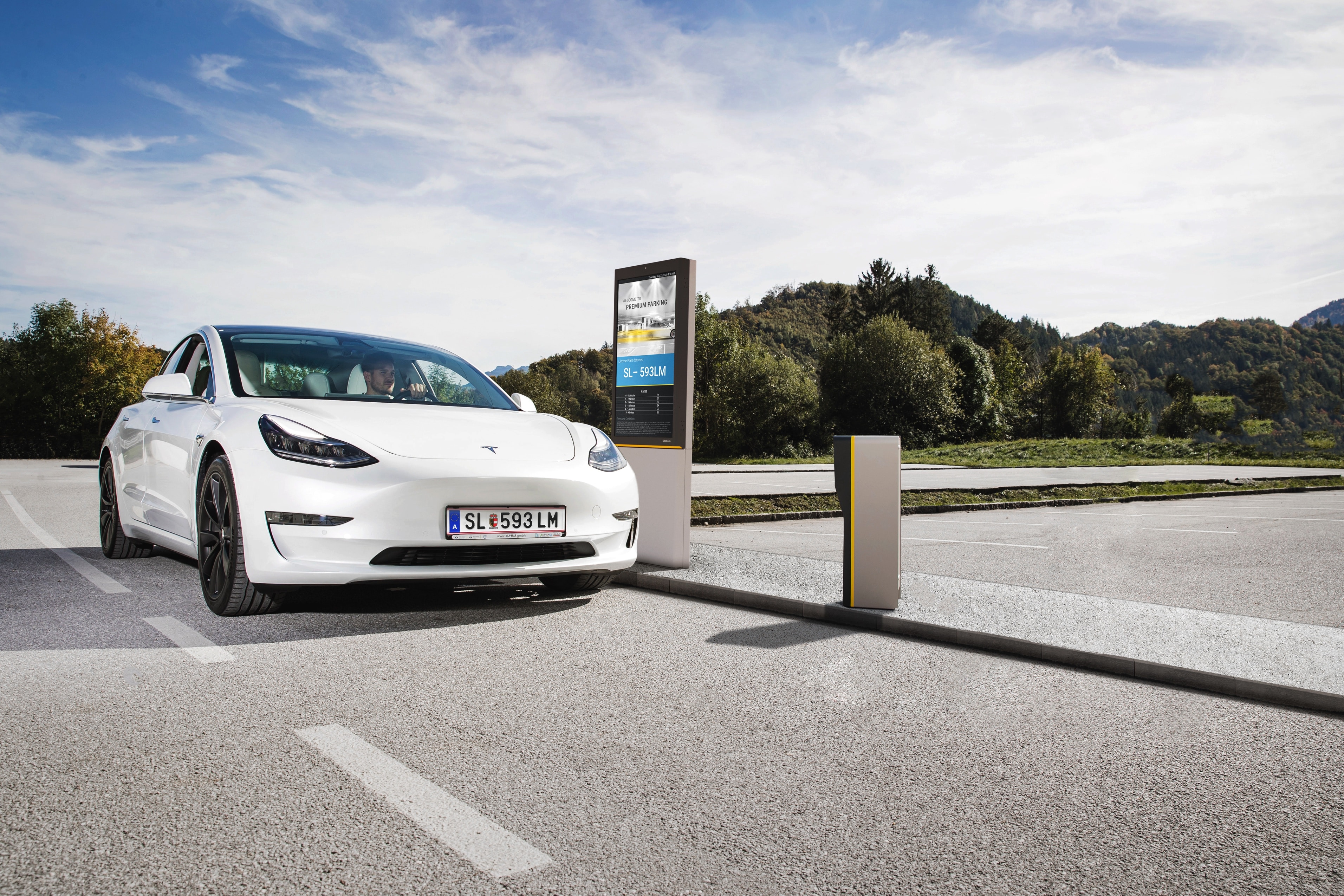 A male is driving an electric vehicle through a digital entrance gate at smart outdoor parking lot with car and parking information shown on gate signage board