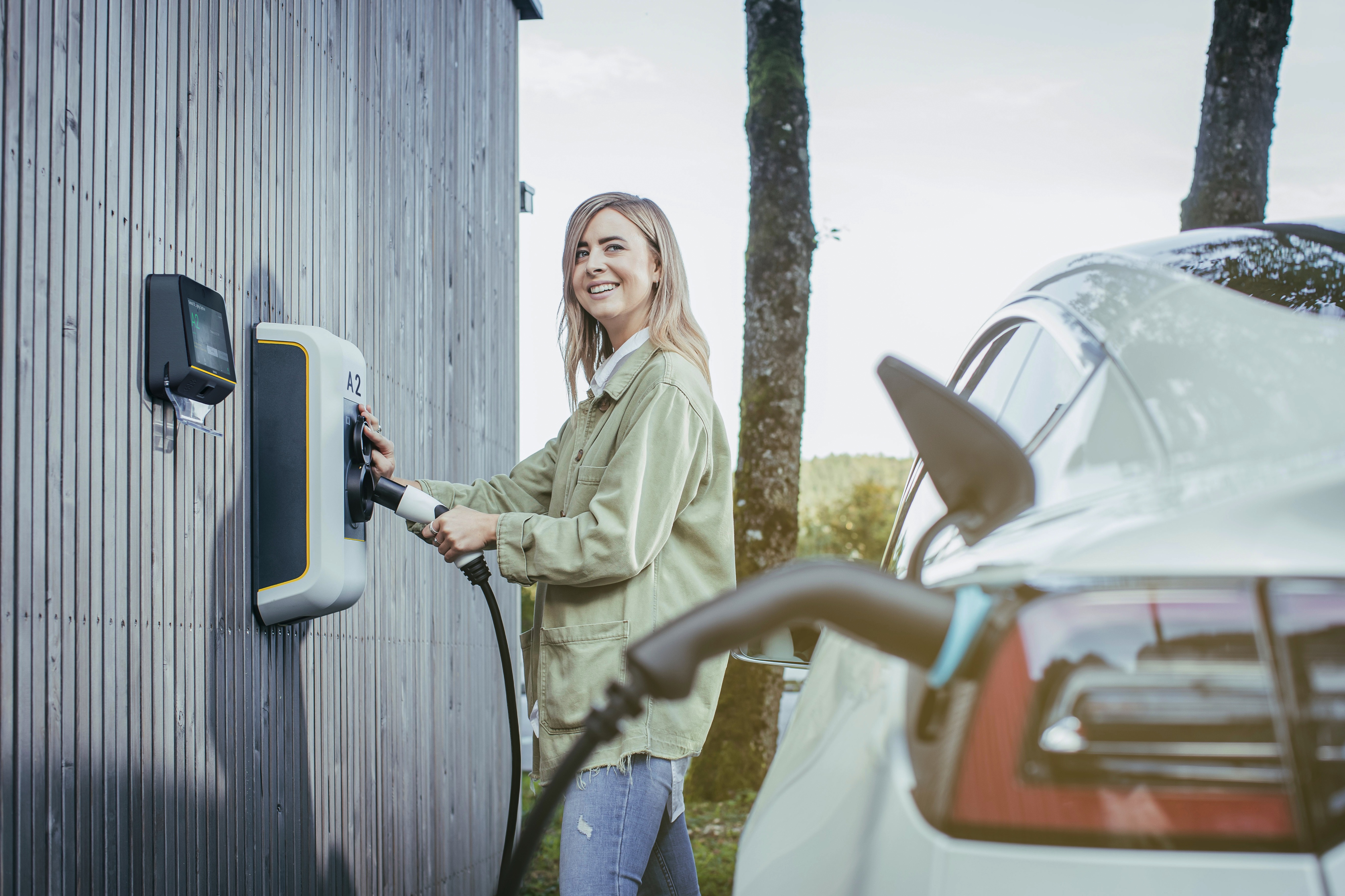 A female is standing at outdoor charging station and holding charging device to power up electric vehicle