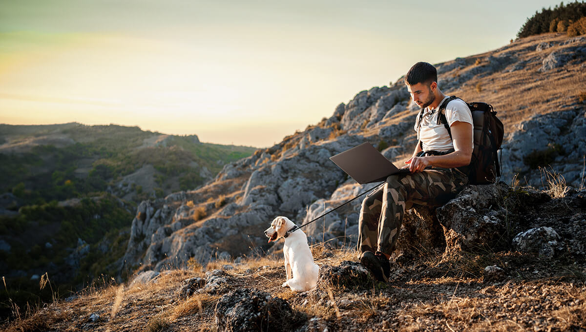 A man is using ProArt P16 while sitting on a rock beside a cliff.