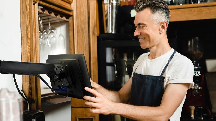 A man wearing black apron using the ASUS ExpertCenter E1 AiO that is mounted in the restaurant wall.